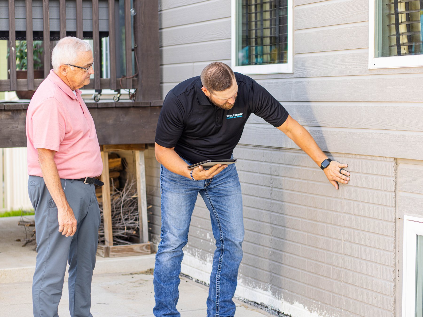 A sales rep with a tablet in hand showing a homeowner a problem on the foundation outside the home